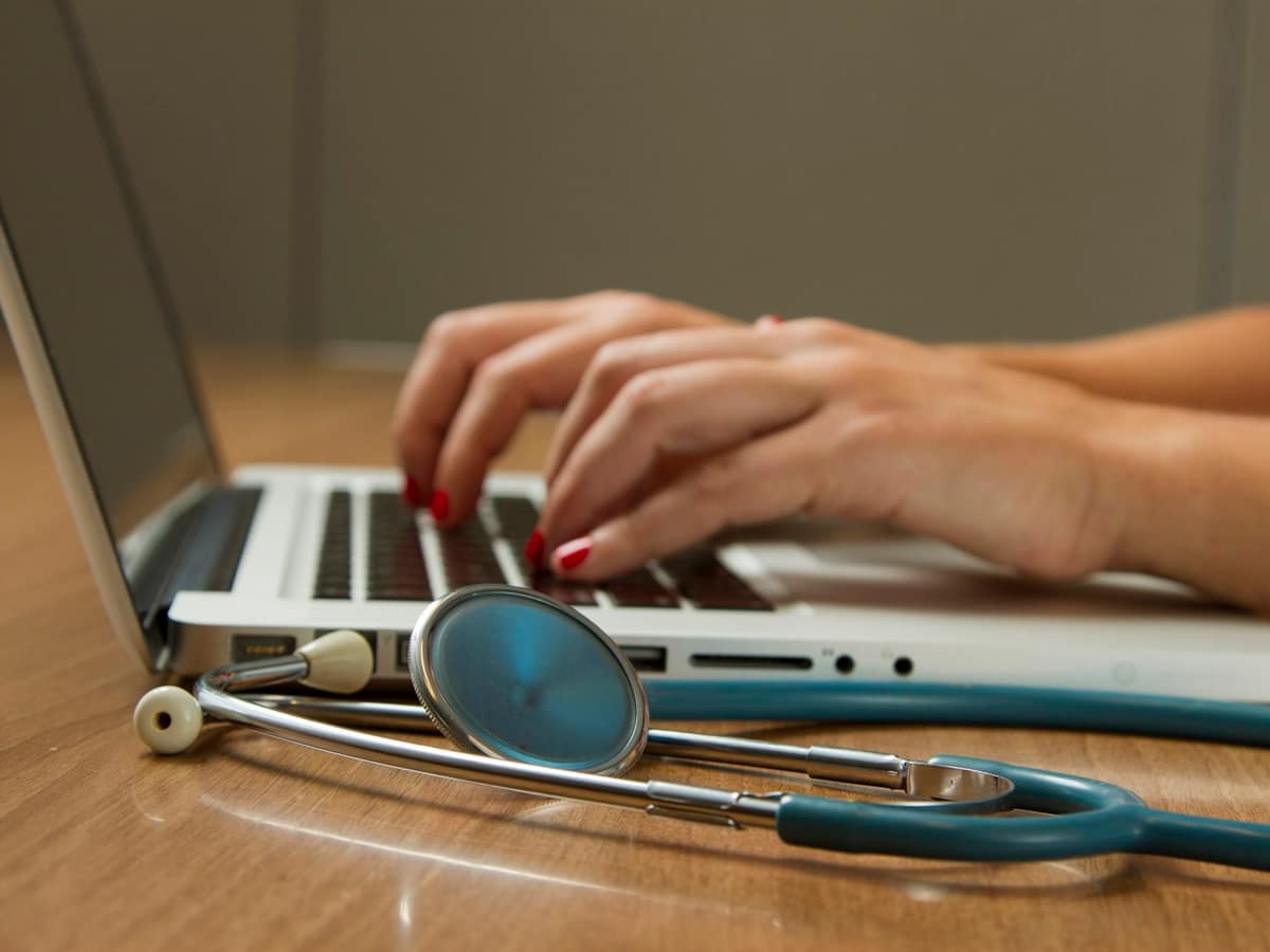 Clinician working on a laptop beside a stethoscope